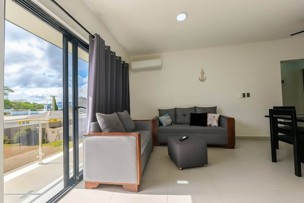 The room is furnished with two contemporary sofas featuring wooden frames and light grey upholstery. One is a two-seater and the other a three-seater, both adorned with decorative throw pillows in muted tones and one black pillow.
