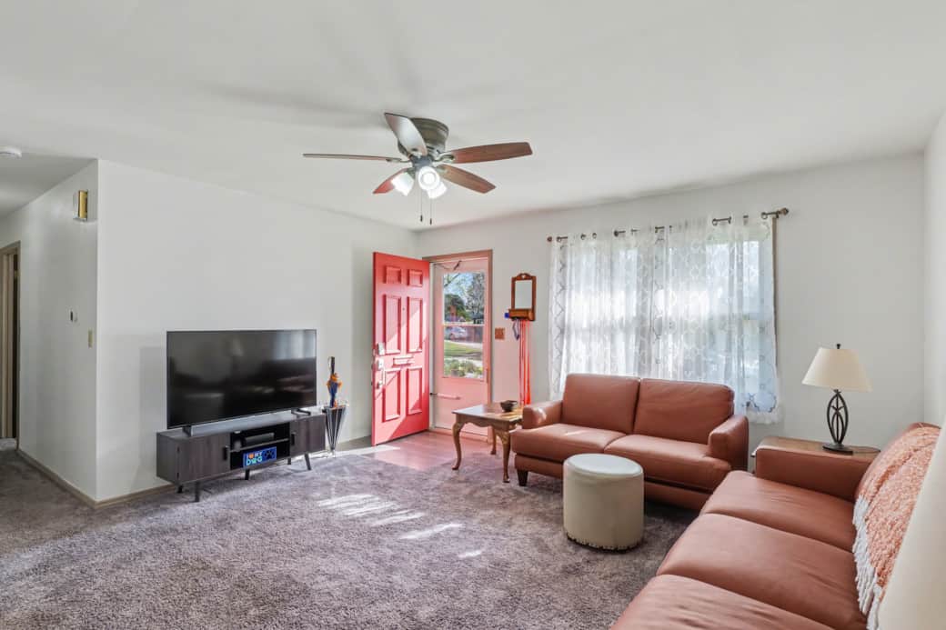 Living room with seating for 6, a recliner and a large Roku TV. Hallway to the bedroom on the right.
