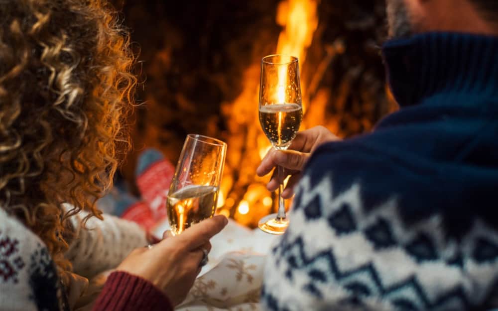 Couple toasting with champagne beside a crackling fireplace