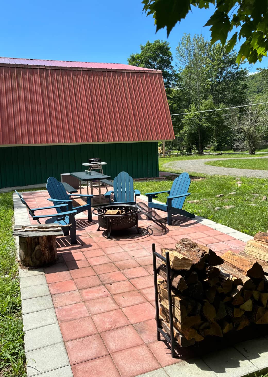 Shared outdoor patio with Adirondack chairs, fire pit, grill, and wooded yard.
