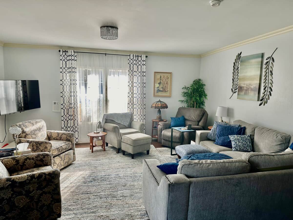 This is a large, comfortable living room with four chairs and a sectional sofa with nice pillows for lounging. There is a 55" TV mounted on the wall.