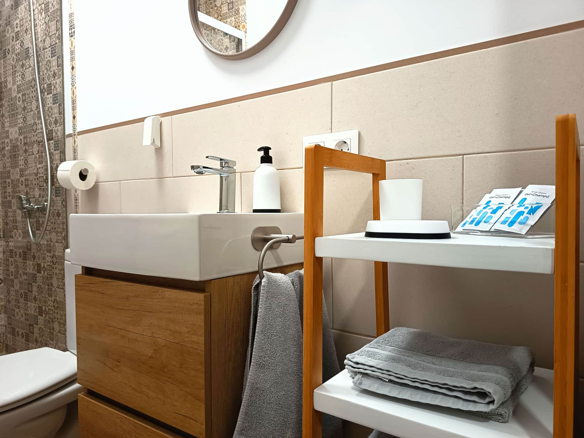 Baño moderno con lavabo de cerámica, mueble de madera, espejo redondo y ducha con azulejos decorativos