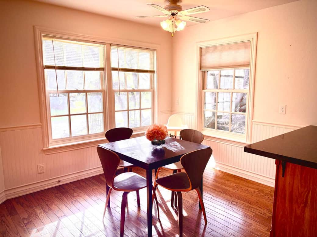 Sunlit breakfast room with wooden dining set for 4. Large windows showcase tranquil woodland views. Airy, peaceful spot for morning coffee and breakfast.