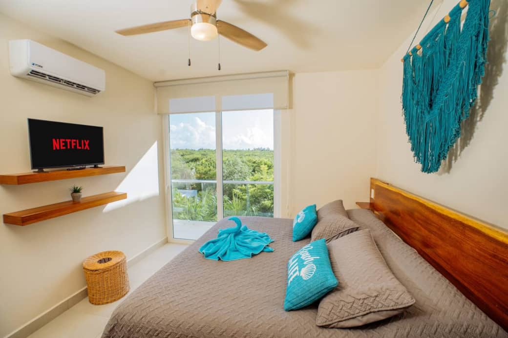 The bedroom offers a peaceful retreat with a comfortable king-size bed, a private balcony overlooking the jungle, air conditioning, a ceiling fan, and room-darkening shades—perfect for rest, relaxation, and a great night’s sleep.