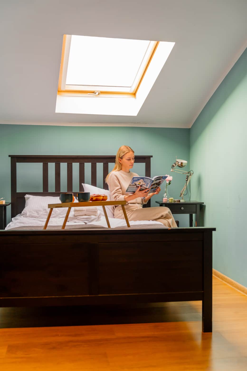 Przytulna sypialnia z ciemnym, drewnianym łóżkiem pod oknem dachowym.