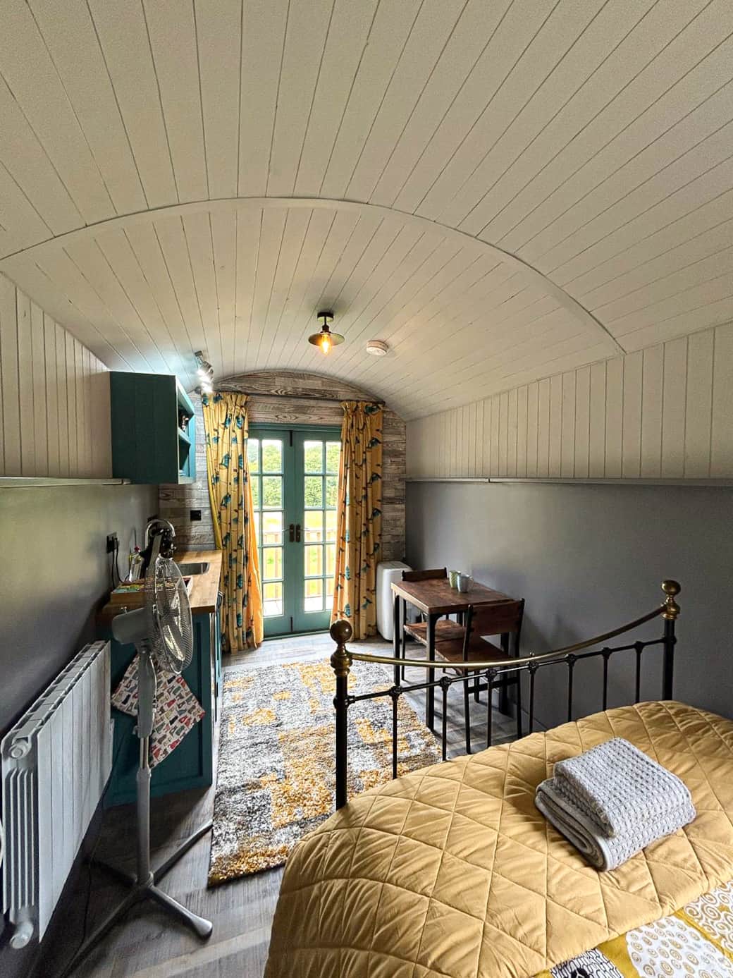Cosy open-plan interior with double bed, dining space and garden views through French doors.