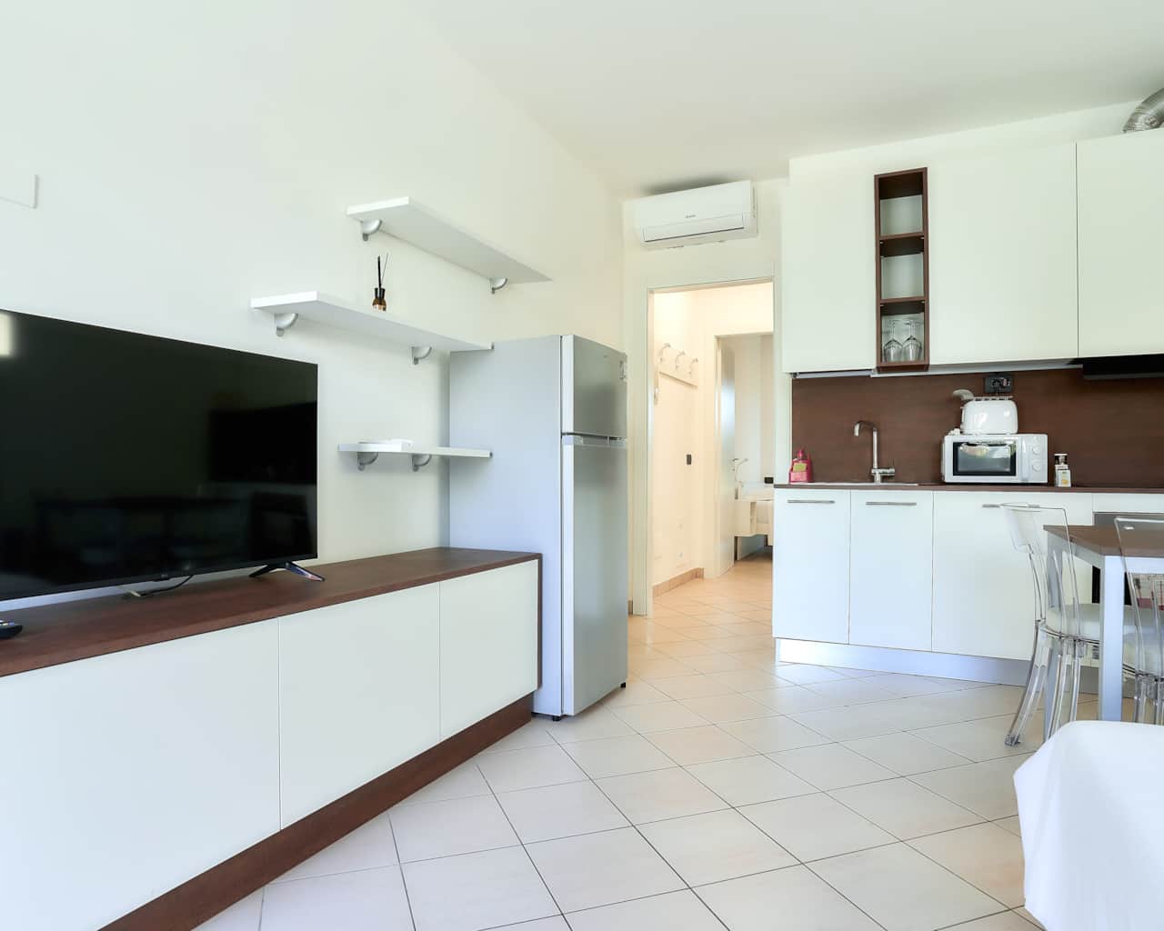 Salón con TV, frigorífico y muebles de cocina blancos, en Monza