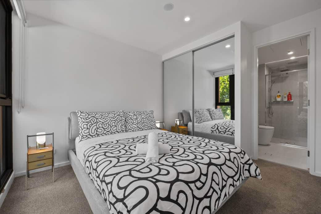 The spacious master bedroom offers a plush queen bed, mirrored wardrobe, and direct access to a private ensuite. Large windows bring in natural light, creating a bright and airy retreat.