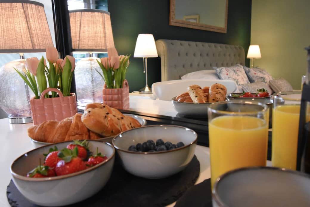 Main bedroom - A cosy, elegant bedroom with a plush super-king bed, floral cushions and soft lighting. Enjoy a peaceful morning with fresh pastries, berries, and juice reflected in a stylish mirror setup — the perfect start to your relaxing stay.