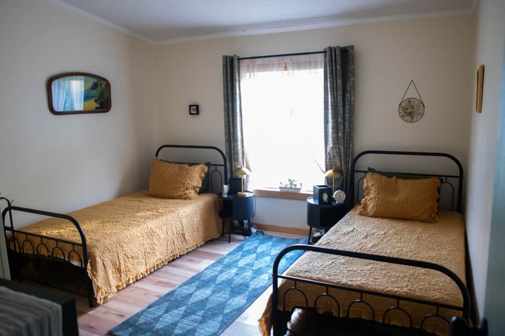 Bedroom 2 sleep two on eco-memory foam beds wrapped in silky bamboo sheets. A green chest, spacious closet, and touch lamps with built-in outlets bring ease and convenience. A graceful towel rack stands ready, completing this peaceful, modern nest.
