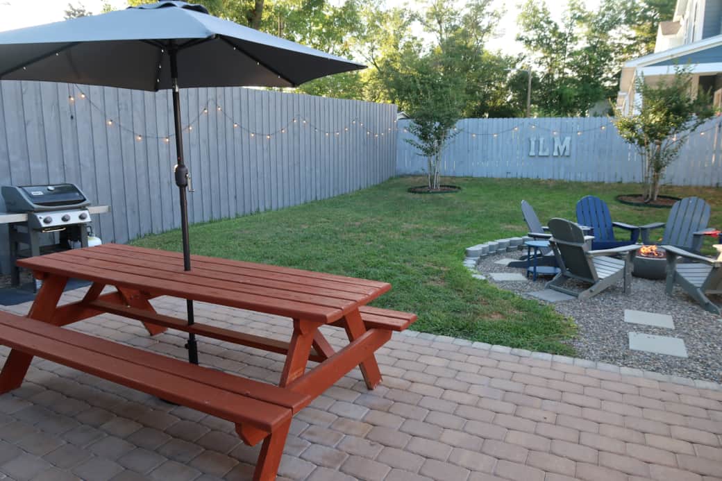Large picnic table with umbrella. Six chairs in the river rock propane fire pit area