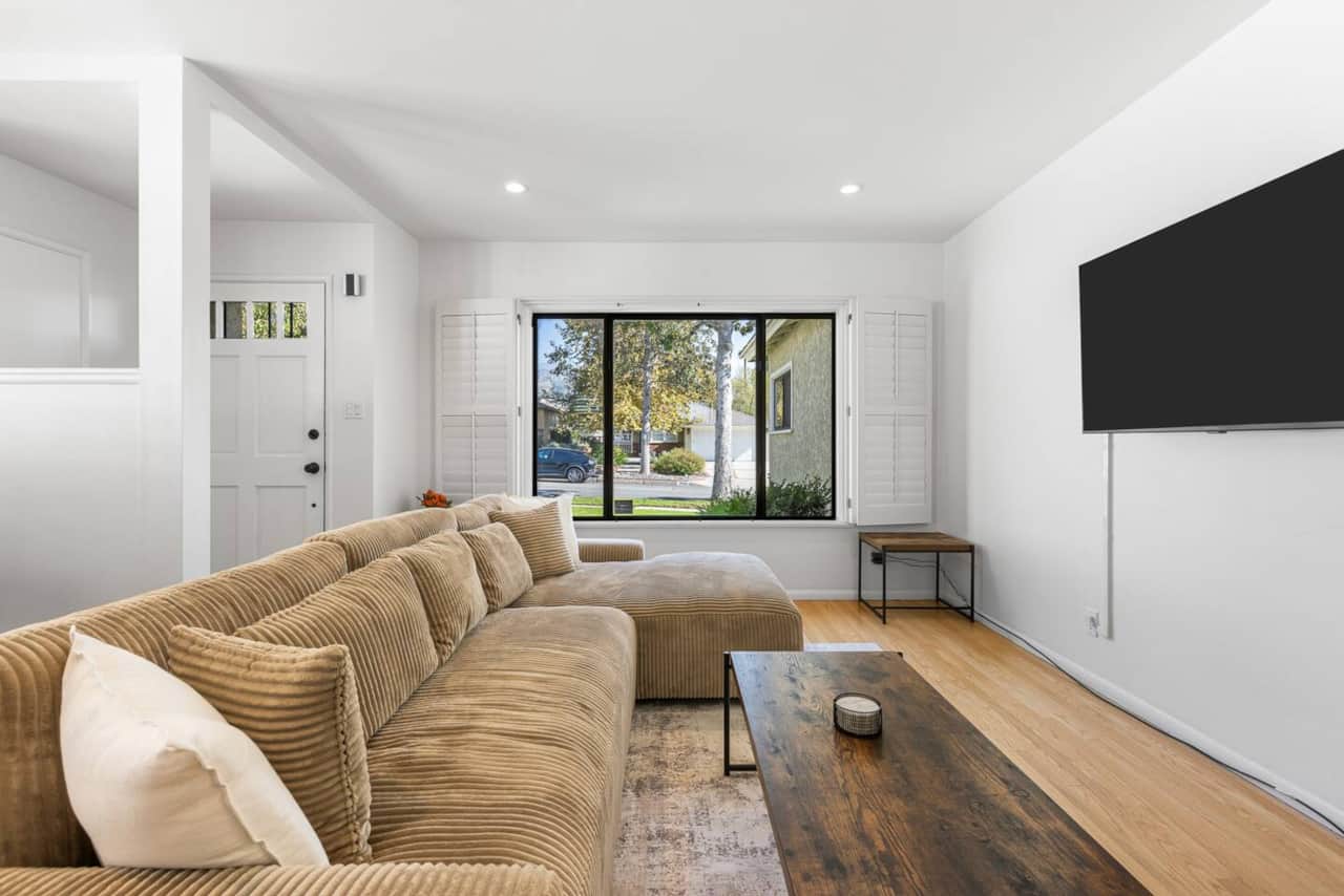 This living room beckons with its cozy sectional, inviting ottoman, and charming patterned rug. 