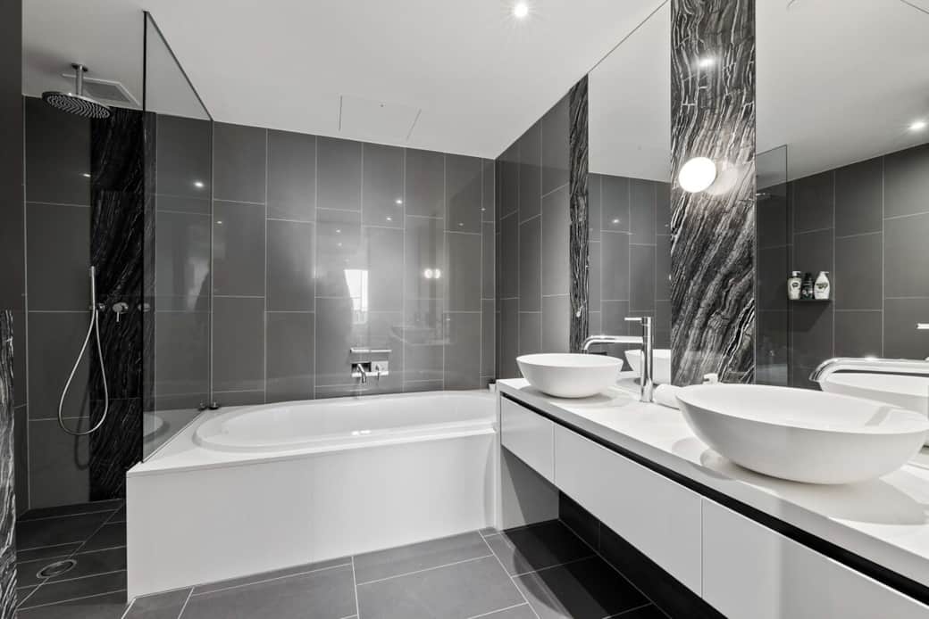 Featuring a large bathtub and dual sinks, it's designed for comfort and convenience. The sleek black tiles and marble accents add a touch of elegance. Enjoy a relaxing bath or a quick shower in this well-appointed space, perfect for unwinding.