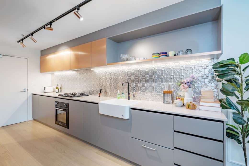 This kitchen showcases a modern design with sleek grey cabinetry and a marble backsplash. The stainless steel appliances and white countertop create a functional and aesthetically pleasing space. A culinary haven for the home cook.