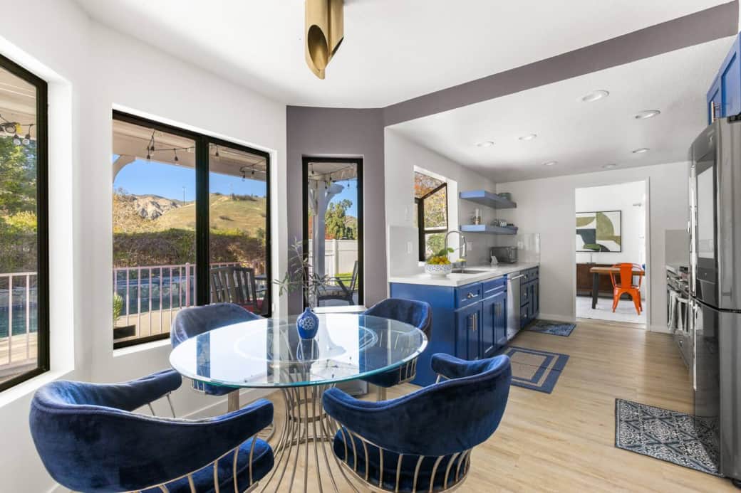 Dining area connects to the blue kitchen with hillside views and expansive windows for seamless flow