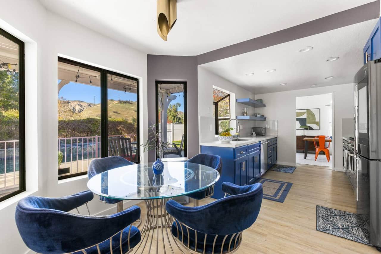 Dining area connects to the blue kitchen with hillside views and expansive windows for seamless flow