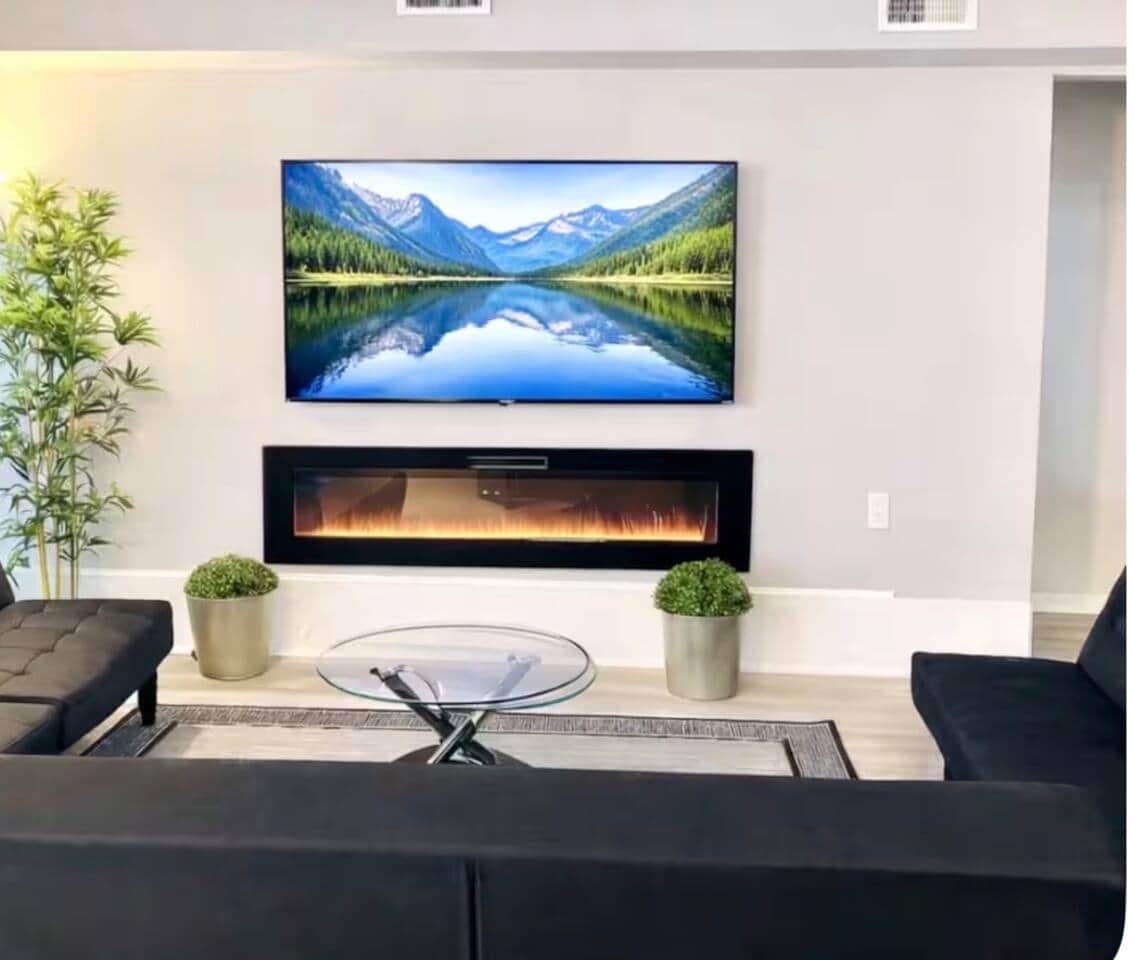Bright, modern living room with three futon sofa beds, an electric fireplace, and a wall-mounted flat-screen TV.