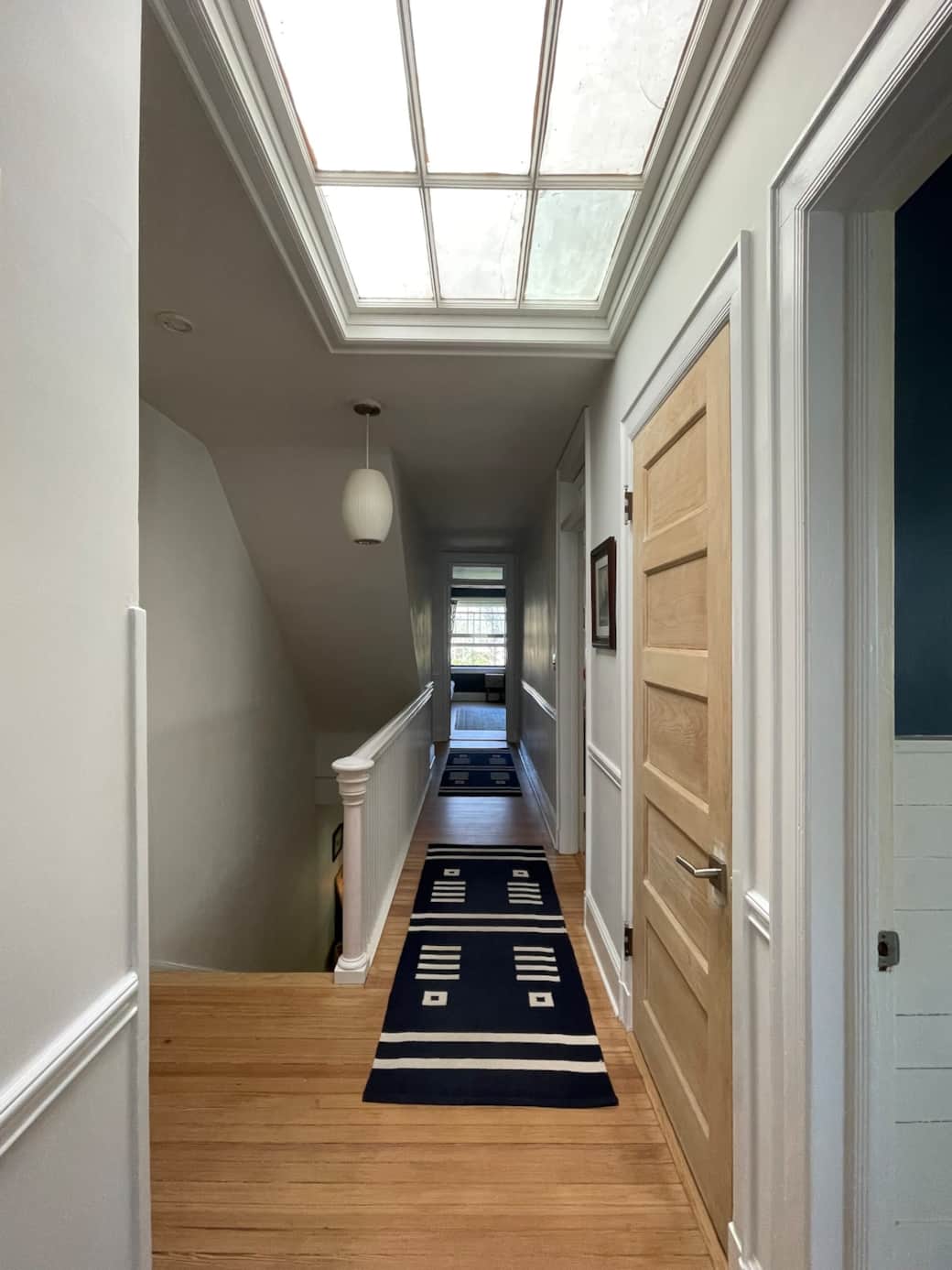 Bright upper hallway with skylight, original trim details, and access to the upstairs bedrooms and bath.