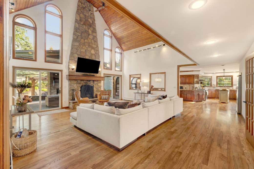 Relax in the elegant living room featuring a vaulted ceiling, grand stone fireplace, and cozy seating. Warm and inviting, it's the perfect space to unwind, connect, and enjoy the morning and evening passing of deer alongside the property.