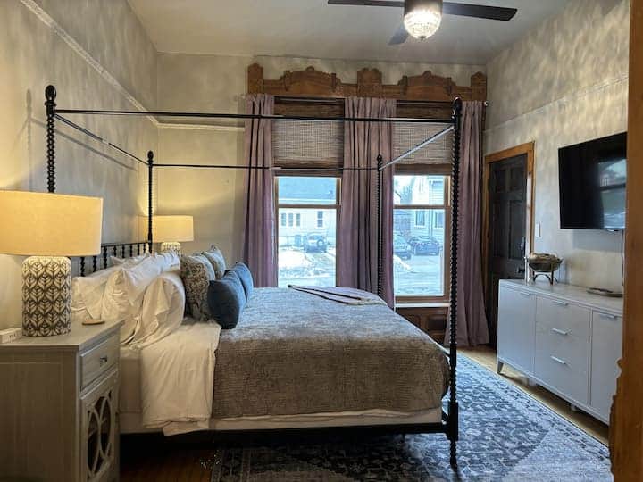 Spacious primary bedroom featuring a stunning four-poster bed, warm ambient lighting.