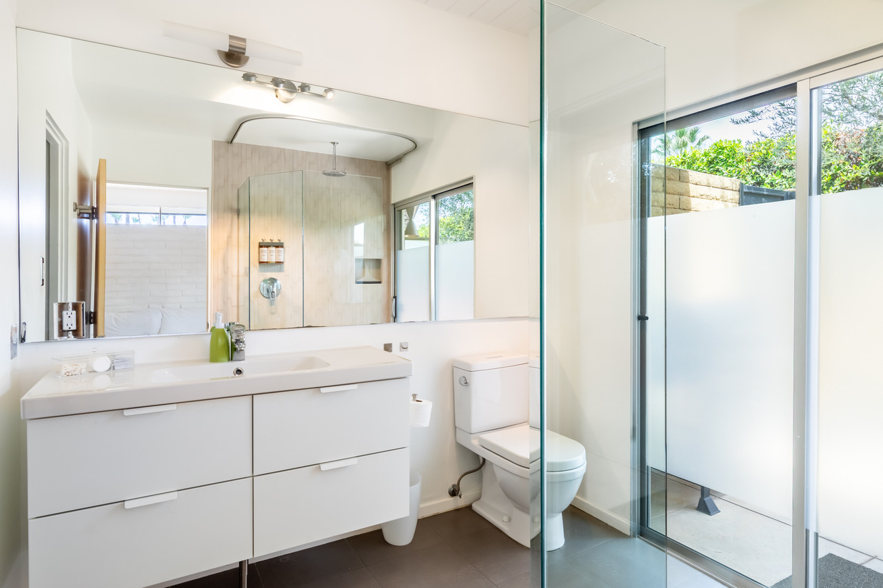 A modern bathroom with a large mirror, double vanity, toilet, and glass-enclosed shower