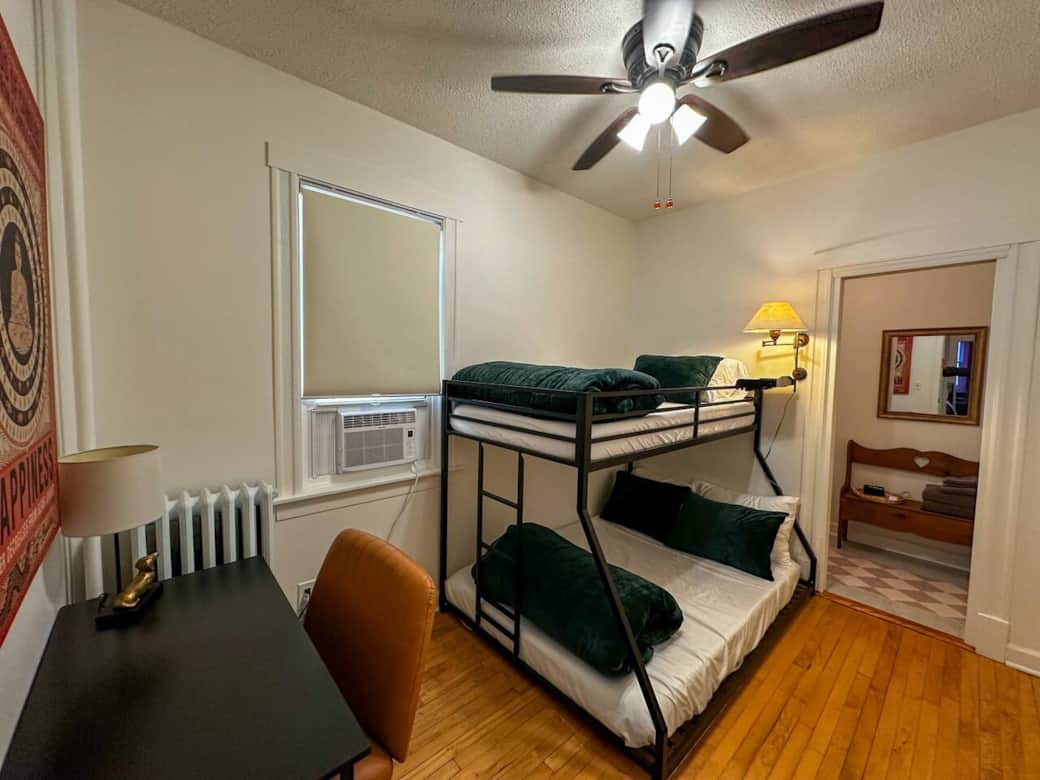 Cozy guest room with a twin-over-full bunk bed, soft green bedding, a work desk, and warm lighting—perfect for kids, friends, or a comfortable night’s rest.