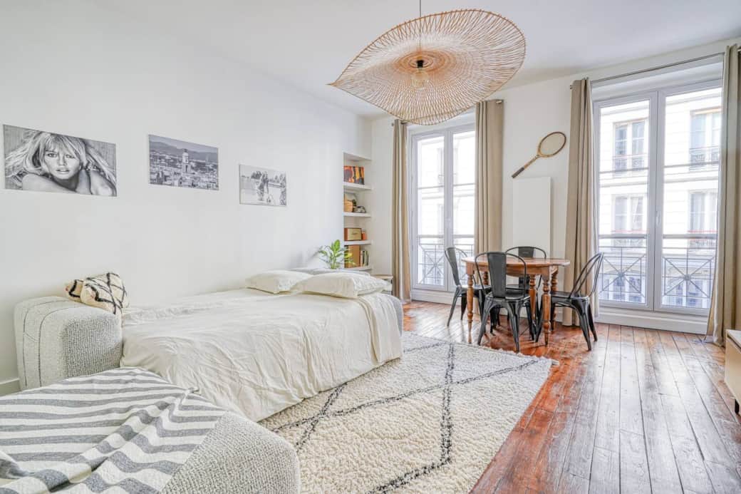 Un espace de vie chaleureux et accueillant, avec un lit confortable, un tapis à motifs géométriques et une table à manger près des grandes fenêtres.