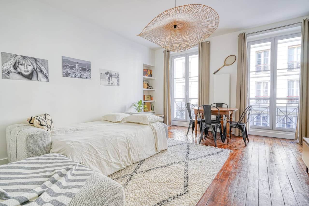 Un espace de vie chaleureux et accueillant, avec un lit confortable, un tapis à motifs géométriques et une table à manger près des grandes fenêtres.