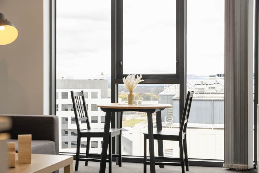 The dining area is a charming spot to enjoy meals, with a table set for four overlooking the city. Natural light floods in through the large windows, enhancing the warm tones of the wooden flooring and creating an inviting space for guests to gather.