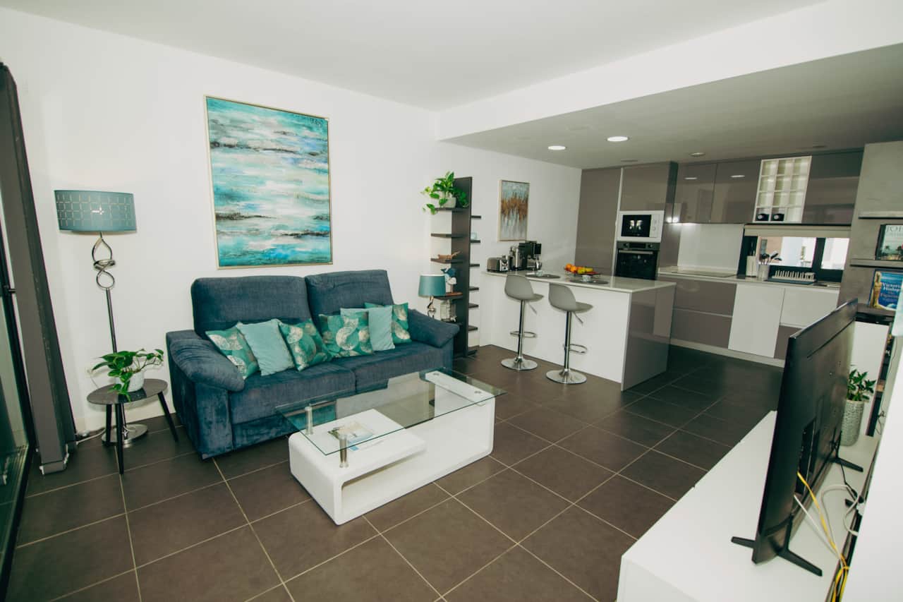 Salón comedor integrado con cocina abierta, isla con taburetes, sofá turquesa y smart TV