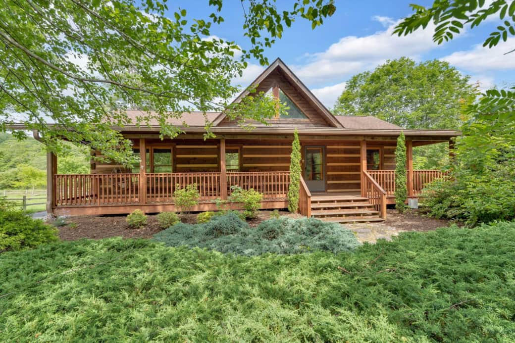Escape to this picturesque log cabin with a welcoming front porch, lush landscaping, and peaceful wooded views. Ideal for relaxing mornings or cozy evenings in nature. Escape to this picturesque log cabin with a welcoming front porch, lush landscaping, and peaceful wooded views. Ideal for relaxing mornings or cozy evenings in nature.
