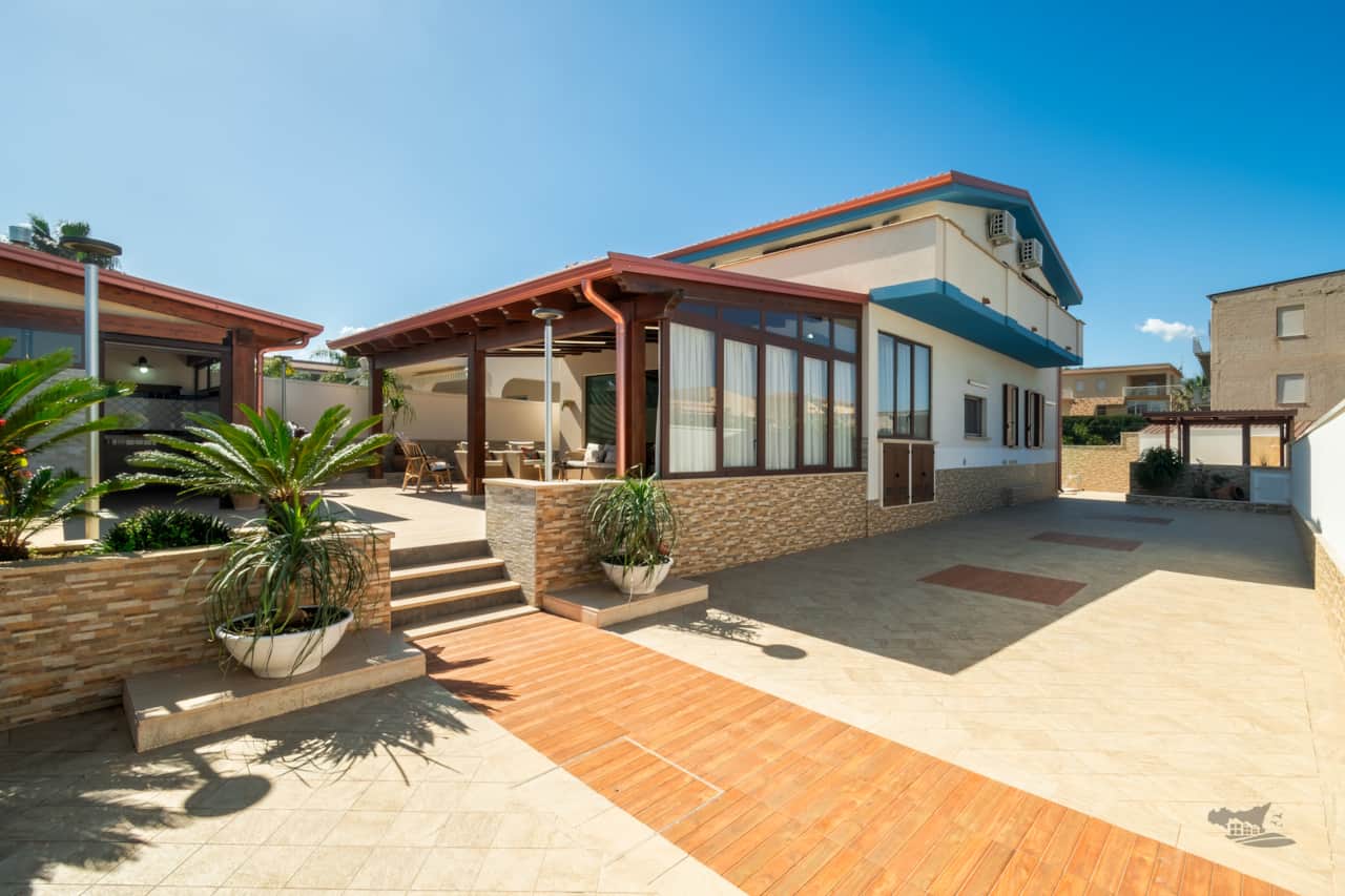 Property overview showing the villa, spacious parking, shaded patio, and outdoor kitchen.