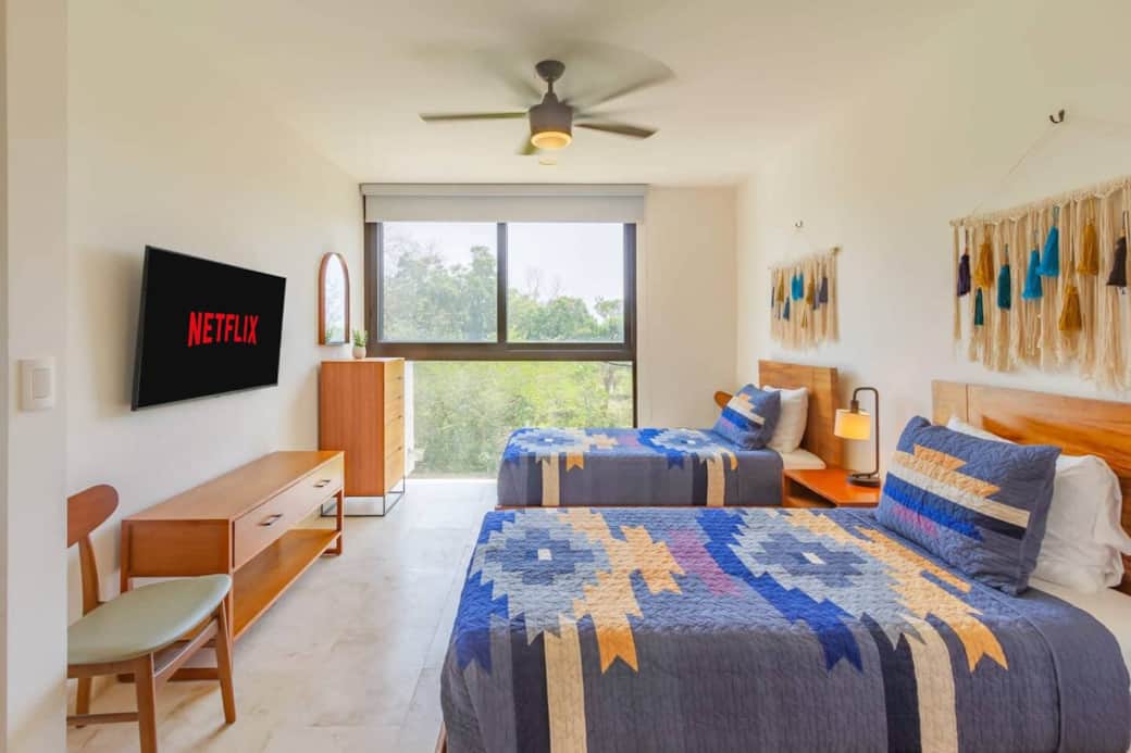 The second bedroom features two twin beds, air conditioning, and a ceiling fan for comfort. Room-darkening shades ensure restful sleep, while large windows offer beautiful jungle views, creating a calm and relaxing space.