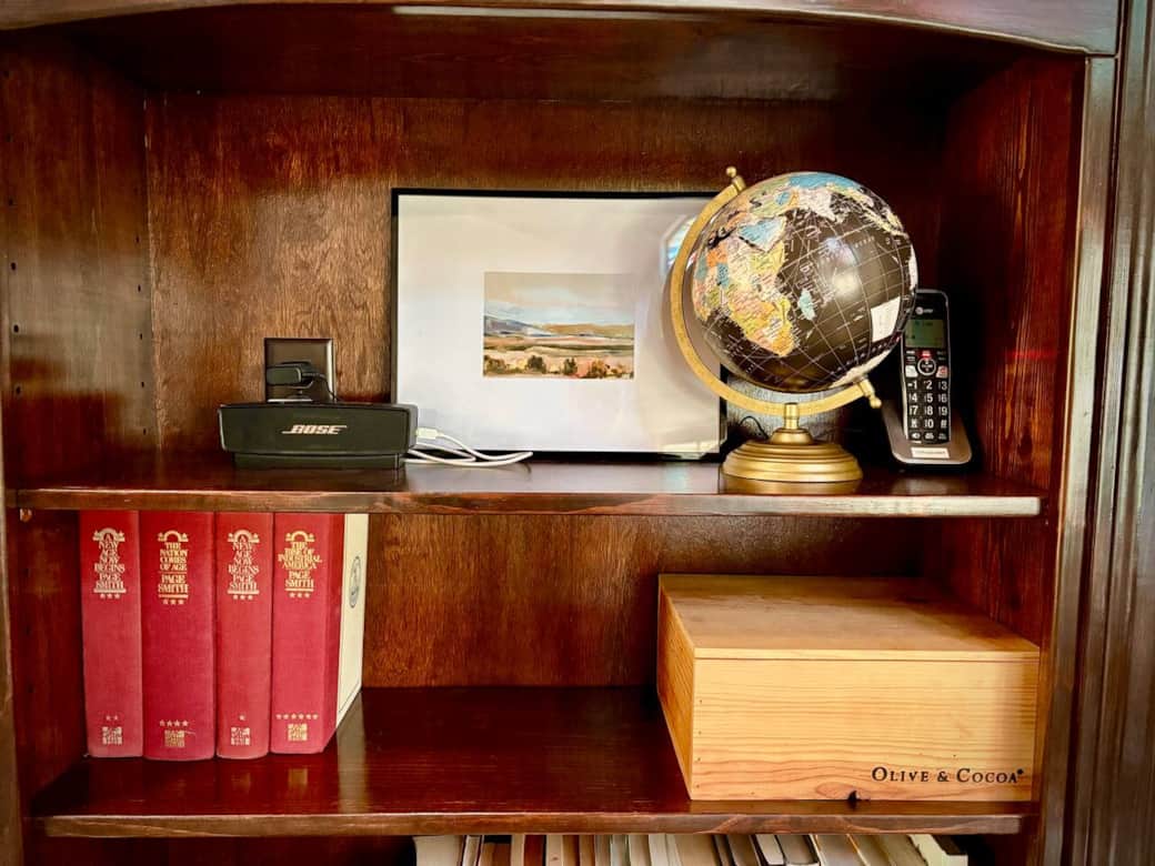 Thoughtfully curated bookshelf with vintage globe and framed landscape art. Rustic wooden shelving adds warmth and character, perfect for quiet reading moments.