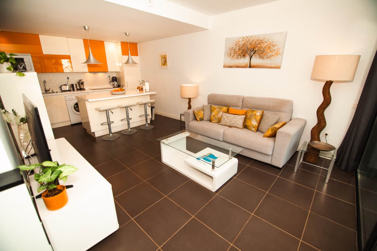 Salón reformado con sofá amplio beige, cojines dorados y mesa de centro de cristal