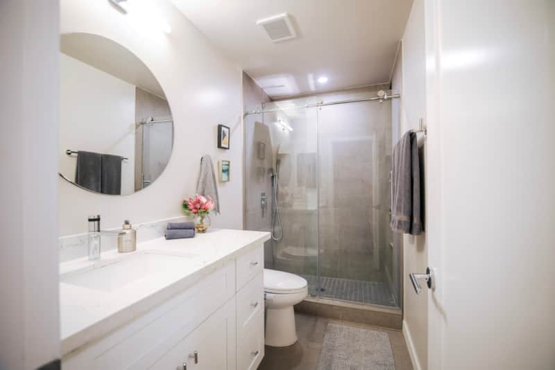 Full bathroom with a vanity, round mirror and glass-enclosed shower.