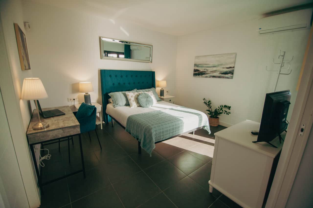 Dormitorio doble con cabecero tapizado turquesa, ropa de cama verde y decoración moderna