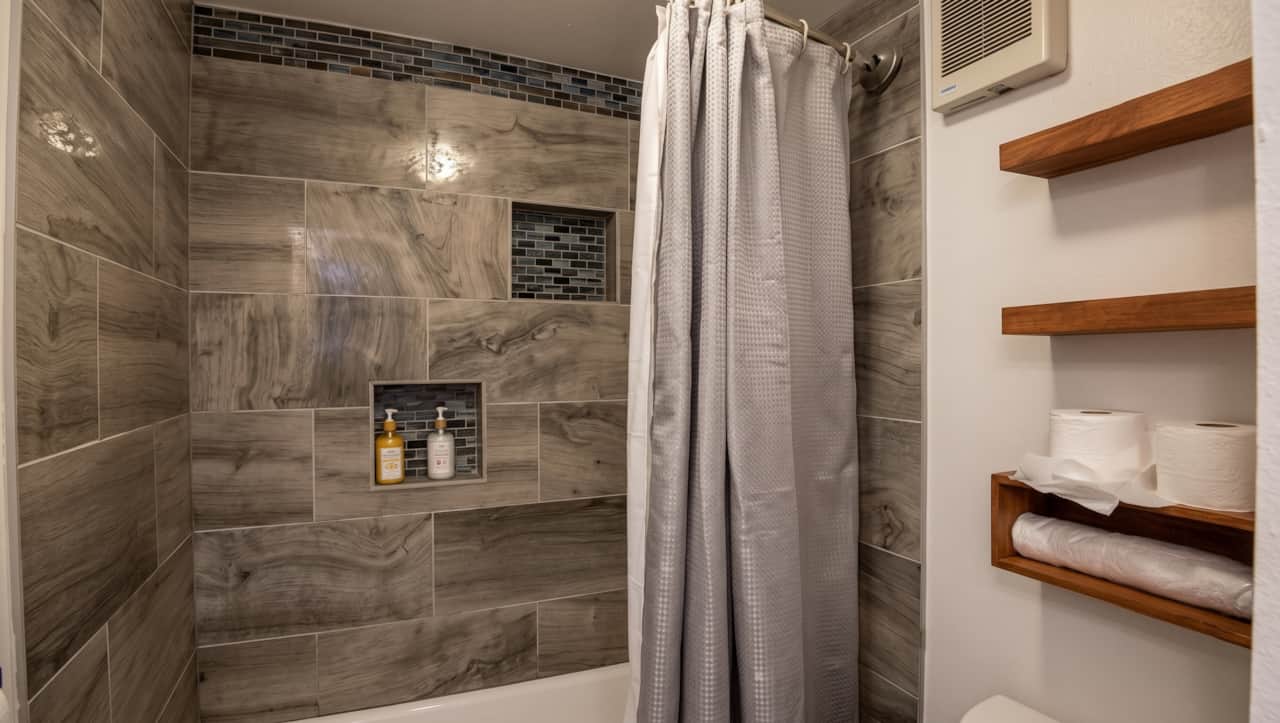 Updated shower and tub area with modern tilework and convenient built-in storage.