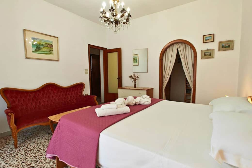 Camera matrimoniale spaziosa con arredi d’epoca e divano elegante, perfetta per vivere il fascino di Siracusa in un appartamento con Wi-Fi e parcheggio privato