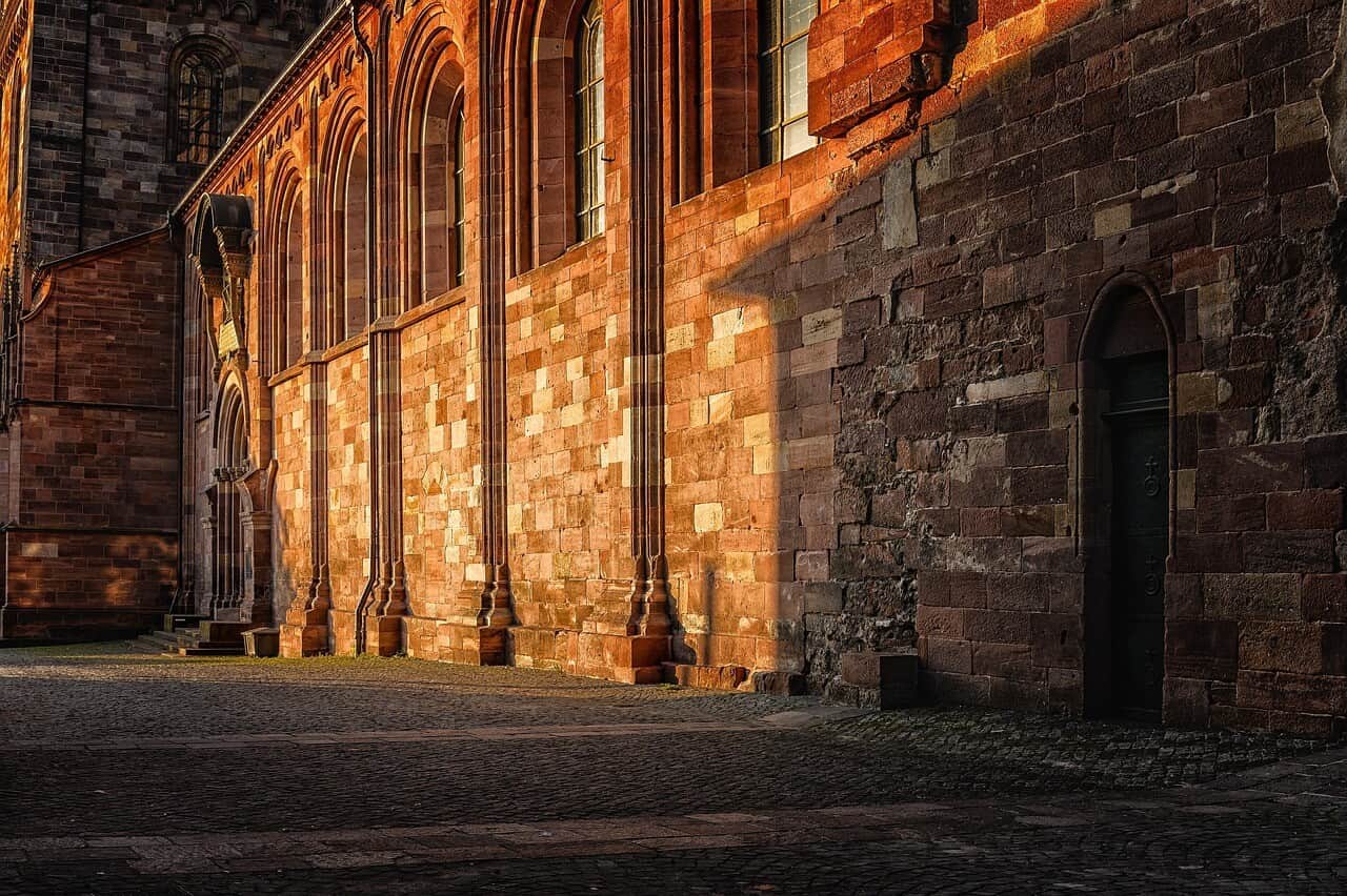 Seitenansicht des Wormser Doms mit Steinmauer und Rundbogenfenstern im Abendlicht.
