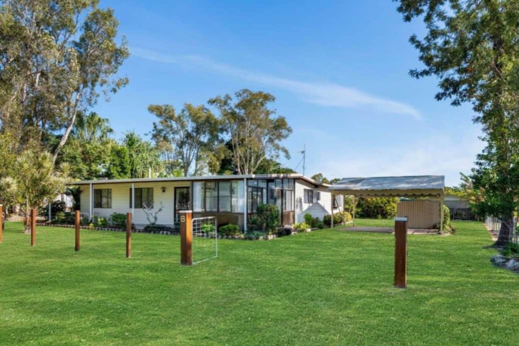 Street-facing view of the property showcasing the large, fully fenced yard. Features include a carport and a sunroom positioned on the front corner.