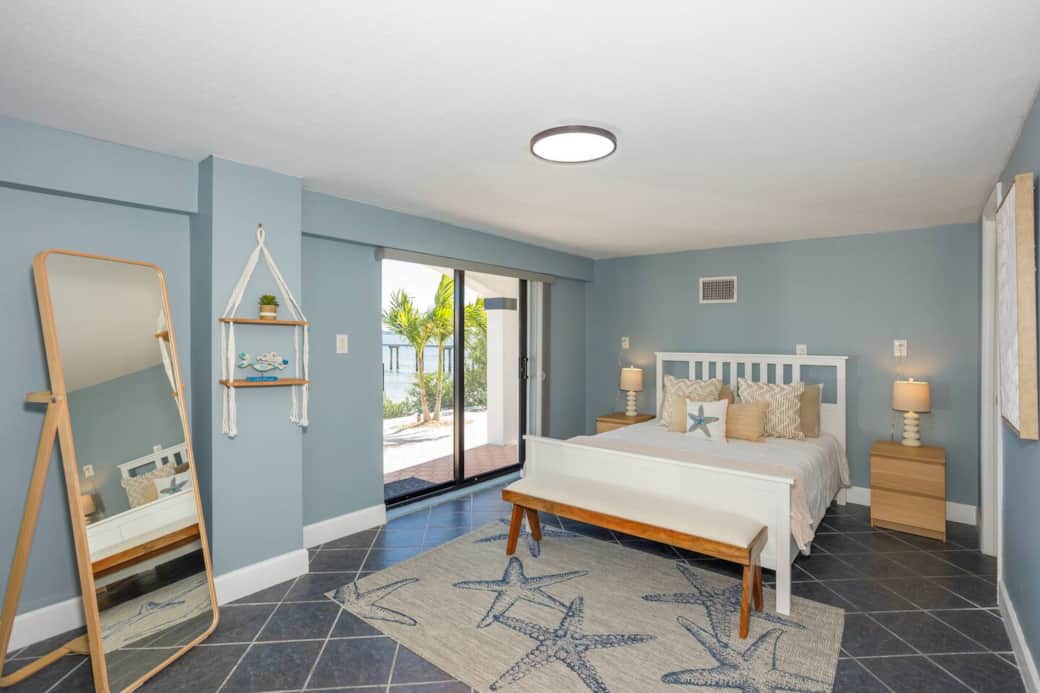 Coastal-designed queen bedroom with sliding glass doors opening to the riverfront.