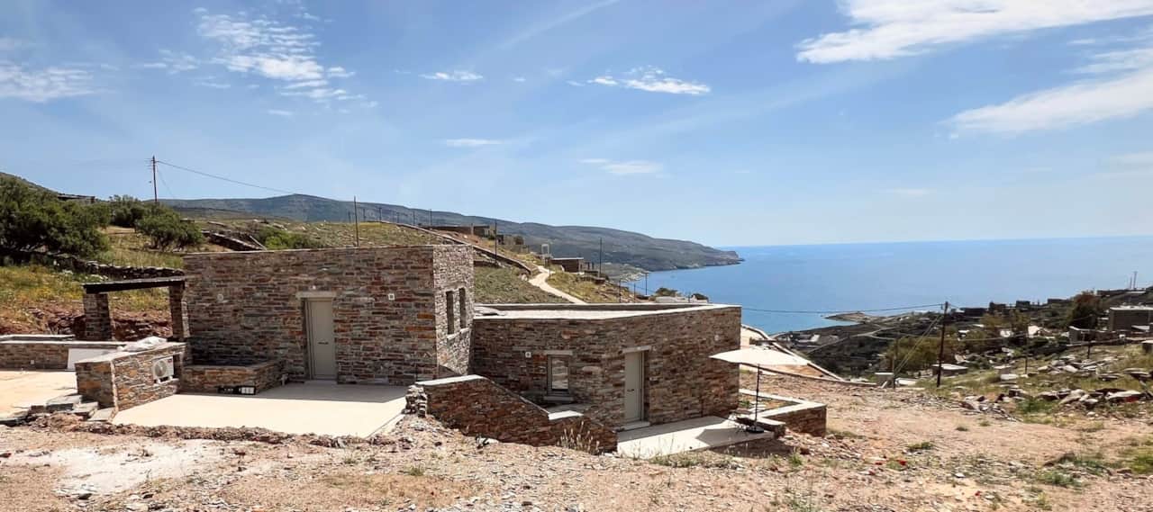 Wide view of two stone holiday lodgings with Aegean Sea and hillside, Koundouros, Kea