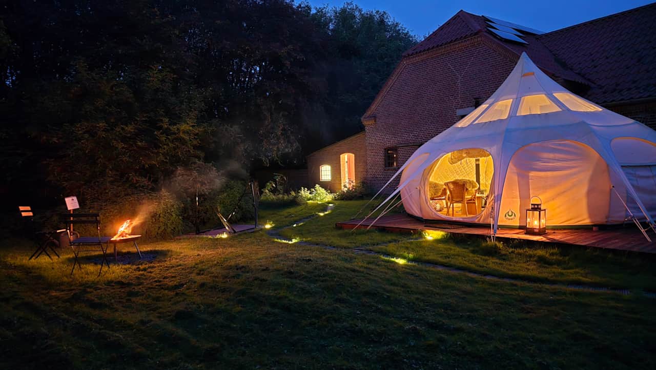 Månefjord Glamping in Roslev – the tent glowing warmly at dusk while the fire burns