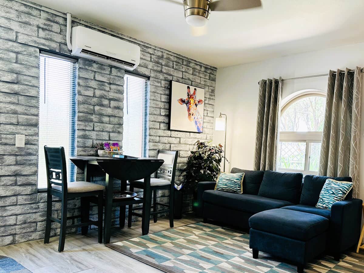 Kameya Casita luxury West Sedona romantic casita rental — plush sectional sofa, drop-leaf dining table, faux brick accent walls, large windows, mini-split AC. Sedona couples retreat steps from Coffee Pot Rock and Sugarloaf hiking trails.