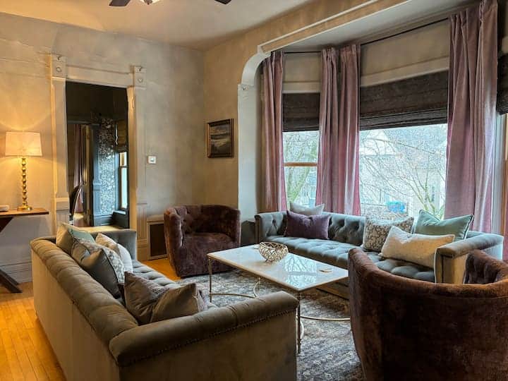 Inviting living room with plush seating, large bay windows, and warm natural light.