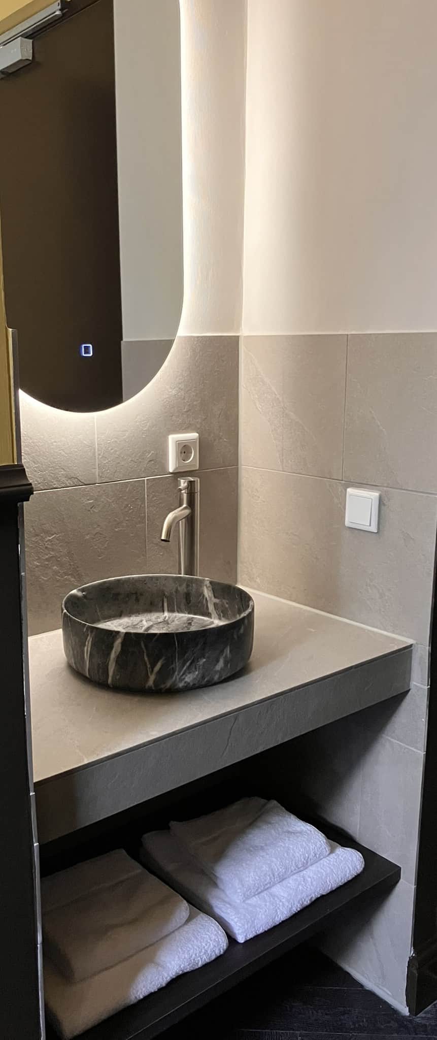 Aleida Suite bathroom vanity with a round stone vessel sink and backlit mirror