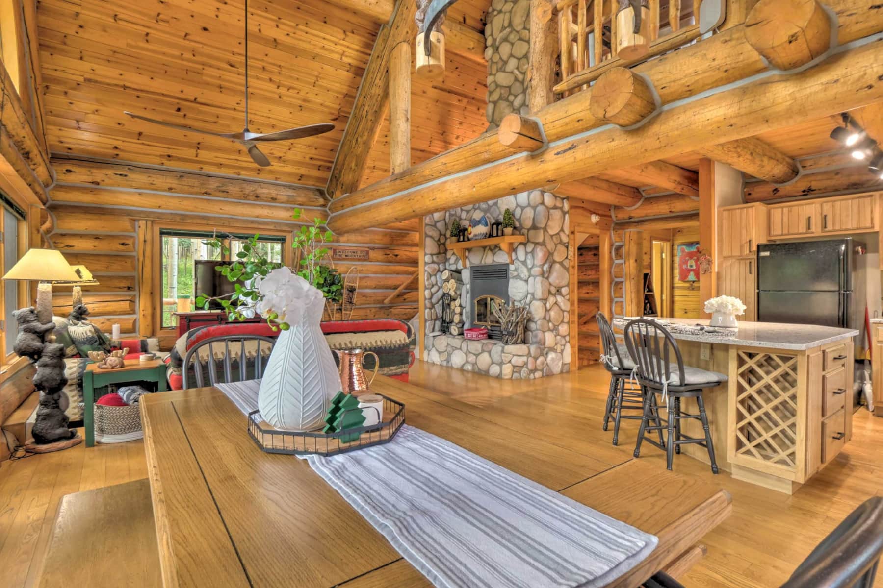 Open-concept great room with a stone wood-burning fireplace and log beams in the Westcliffe cabin