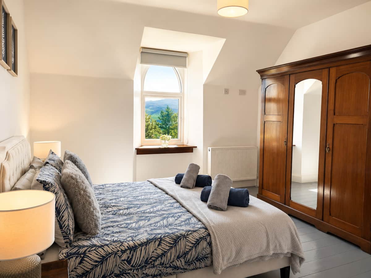 Bedroom 2 with a tall wooden wardrobe and an arched window.