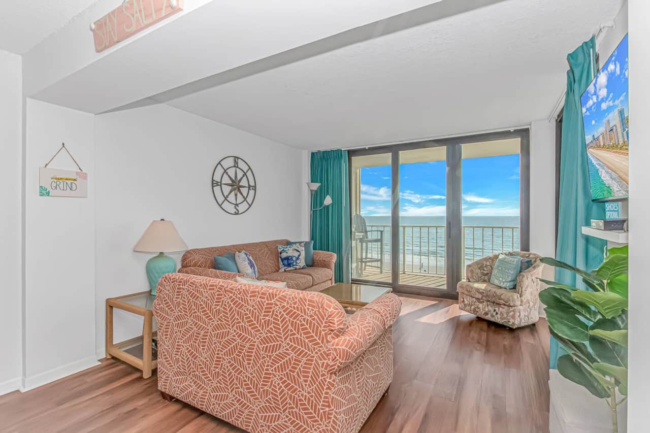 Relax in this airy living room featuring plush seating, coastal décor, and sweeping ocean views from the private balcony.